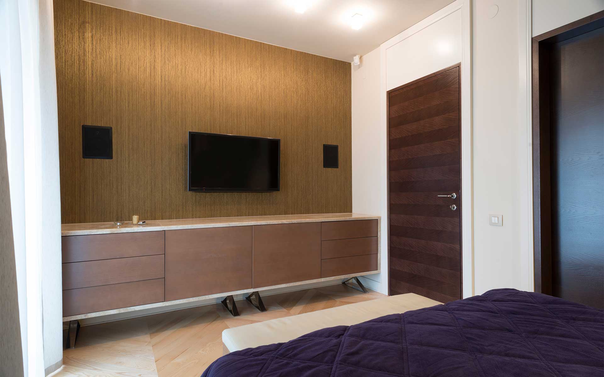 A bedroom featuring a wood-paneled wall with two small in-wall speakers framing a TV