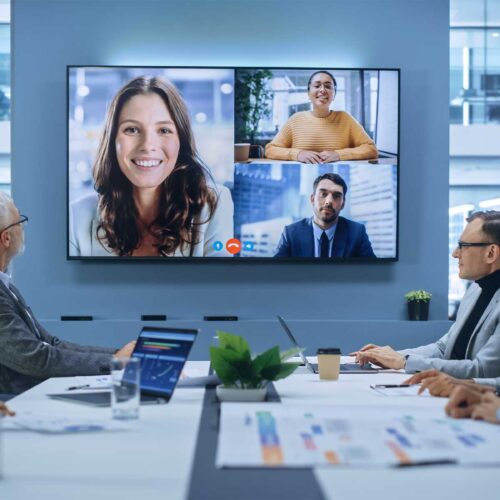 A group of business people sitting around a large conference room table while participating in a video conference meeting