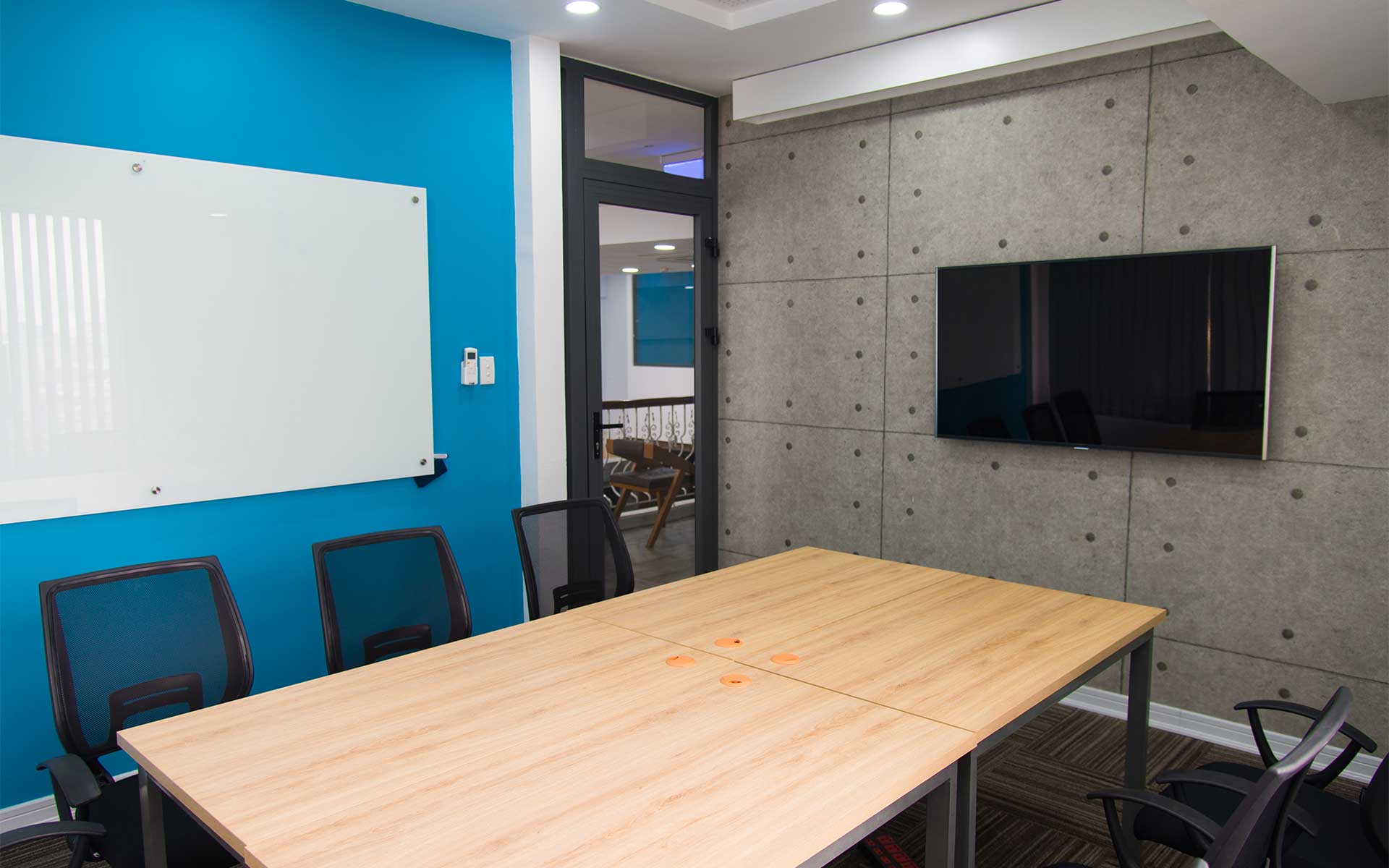 A small conference room with a table, featuring a TV and a whiteboard mounted to the walls