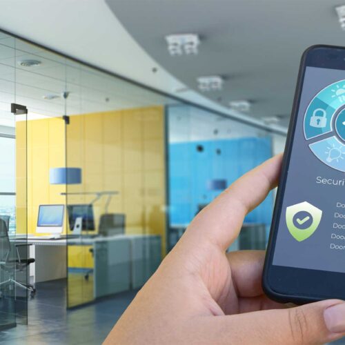 A close-up of a person's hands holding a smartphone displaying a smart office automation app while in an office setting