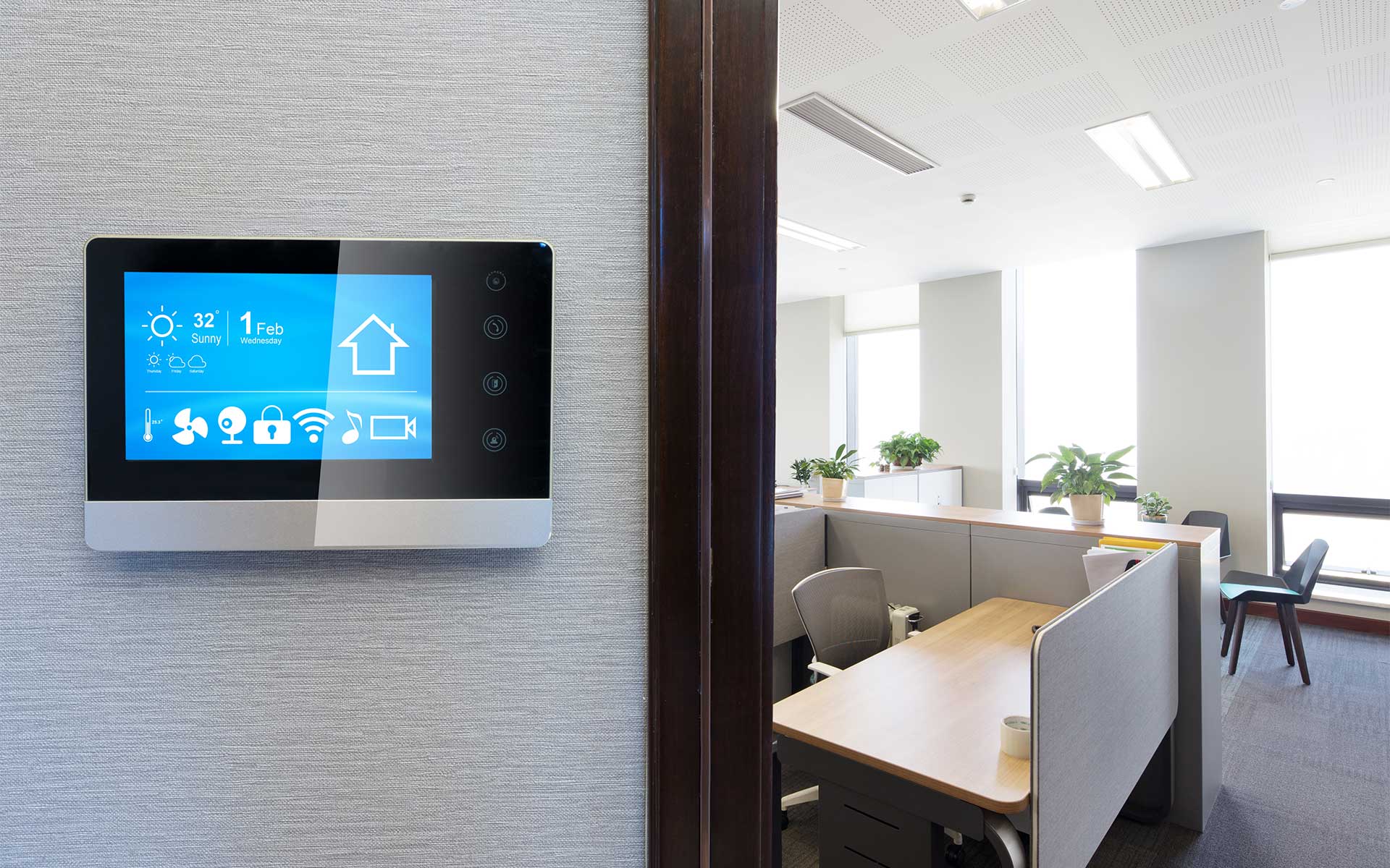 A smart automation control display mounted to a wall outside an office space with cubicles
