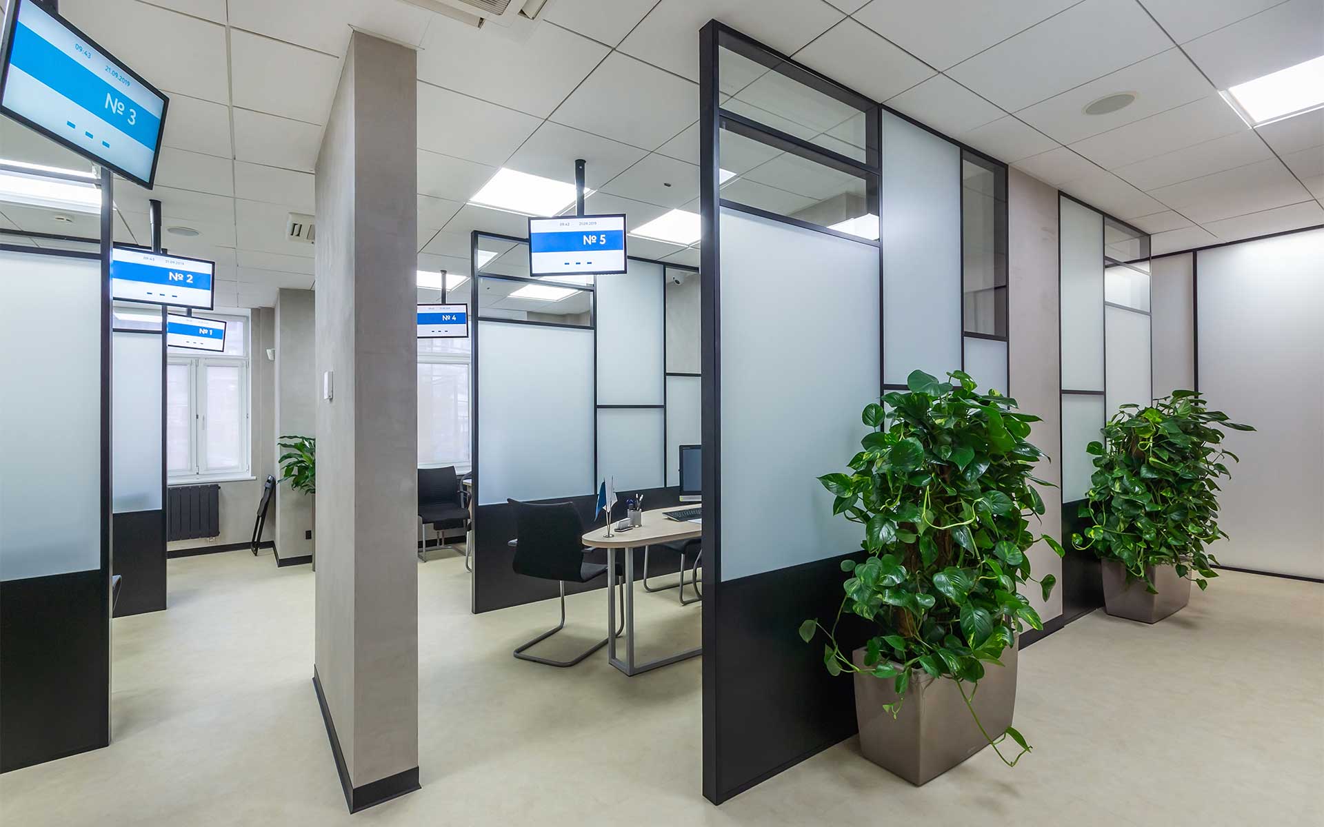 Modern cubicle office layout with high black and white glass panels and ceiling-mounted digital displays