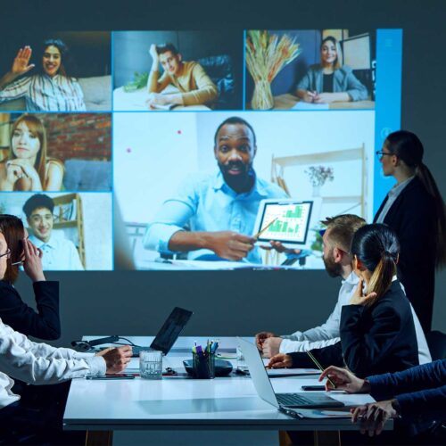 A conference room with business people sitting around a table viewing a large LED screen broadcasting a virtual meeting to demonstrate AV industry trends