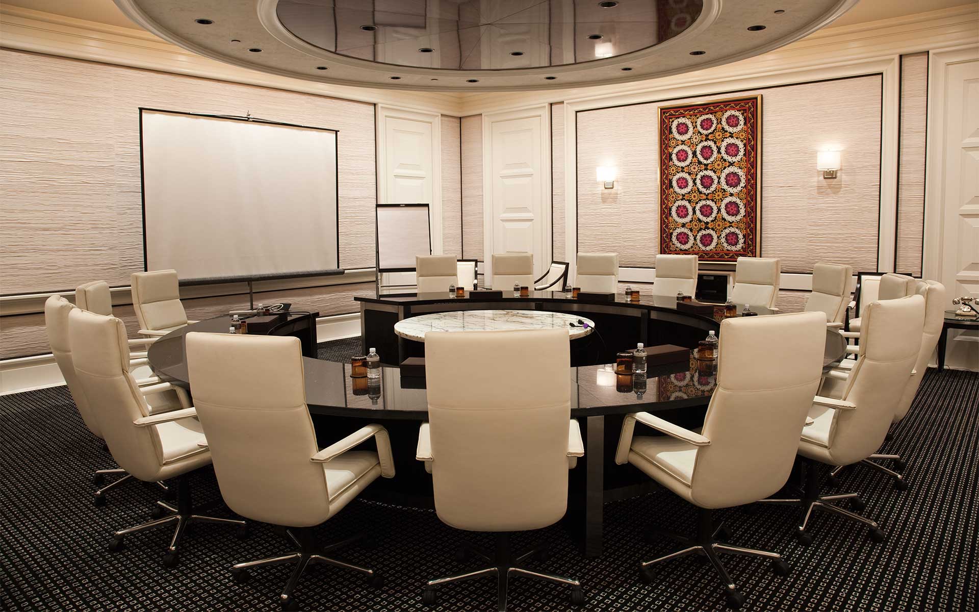 A beautiful modern boardroom in cream colors, featuring a round conference table with multiple chairs facing a large screen
