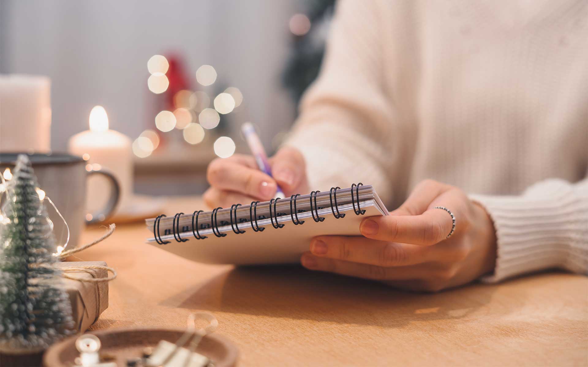 A woman sitting at a table decorated for the holidays, holding a notepad and pen for making a checklist
