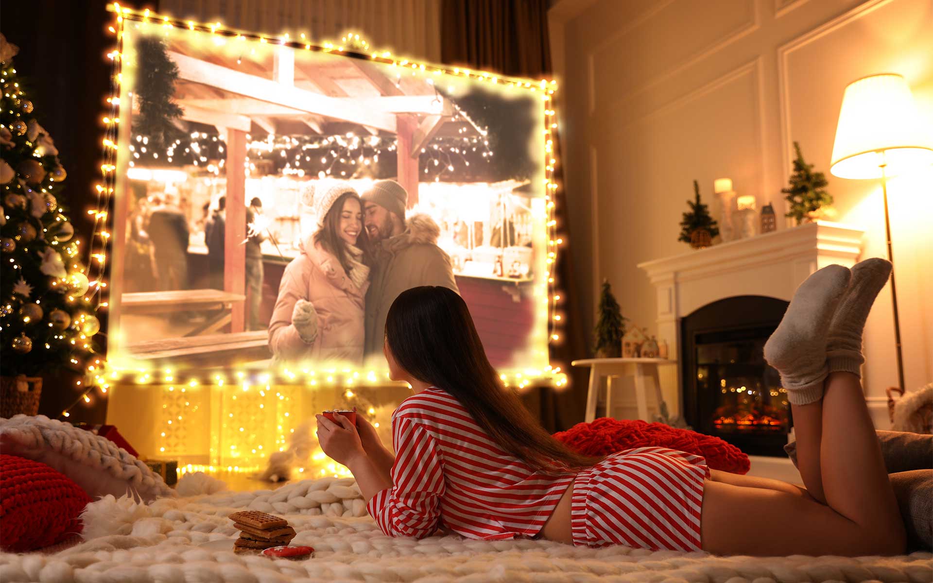 A woman lying on a cozy blanket watching a movie projected on a large screen in a living room decorated for the holidays