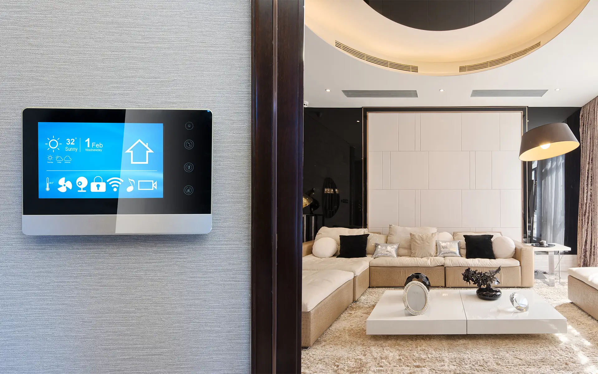 A smart home automation control pad on the wall adjacent to the entry into a modern, luxury living room