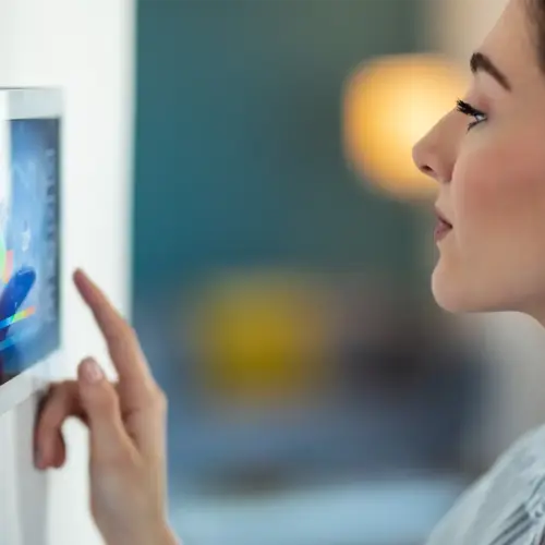 A woman with dark hair adjusts her home's temperature using a smart home automation control panel