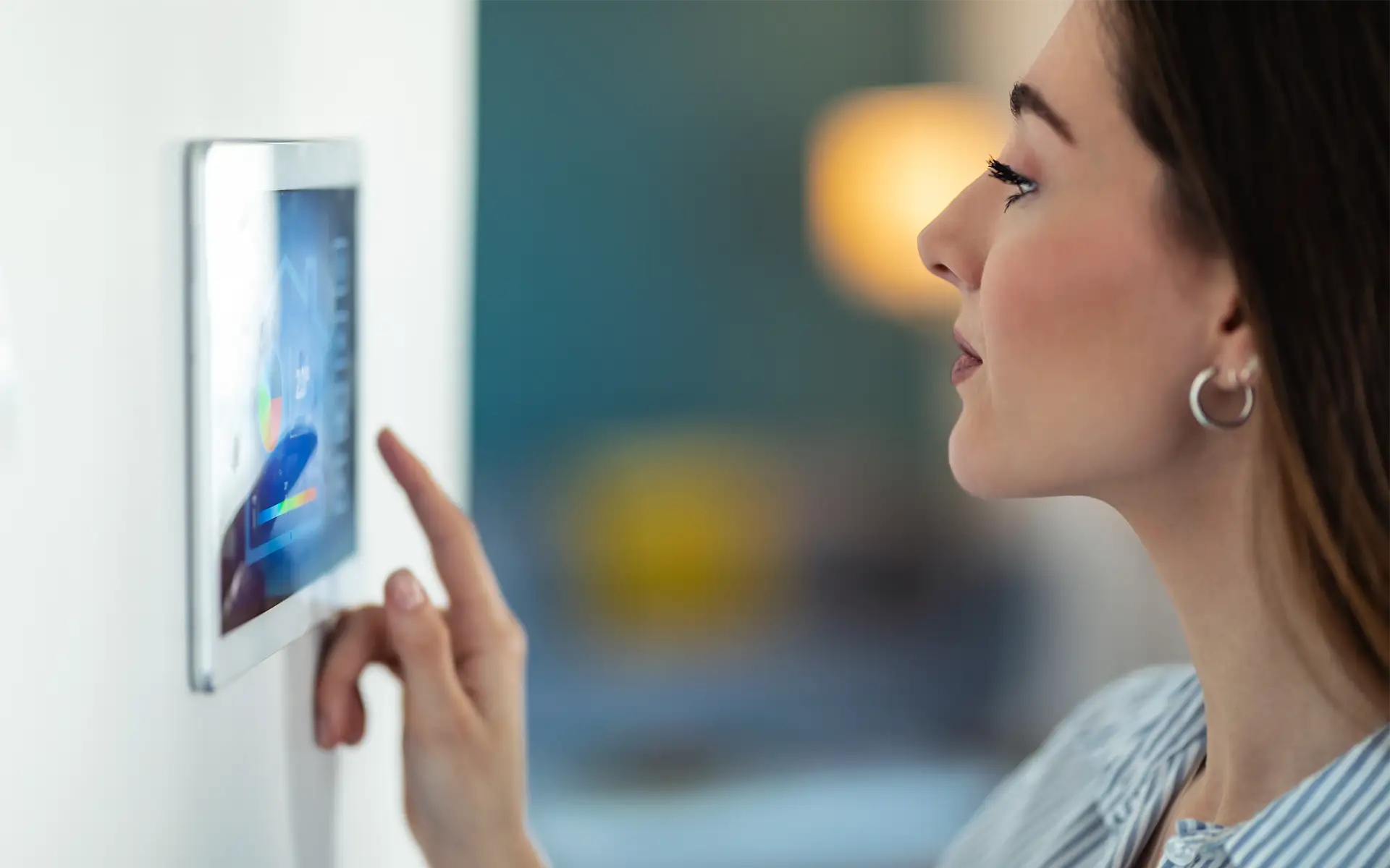 A woman with dark hair adjusts her home's temperature using a smart home automation control panel