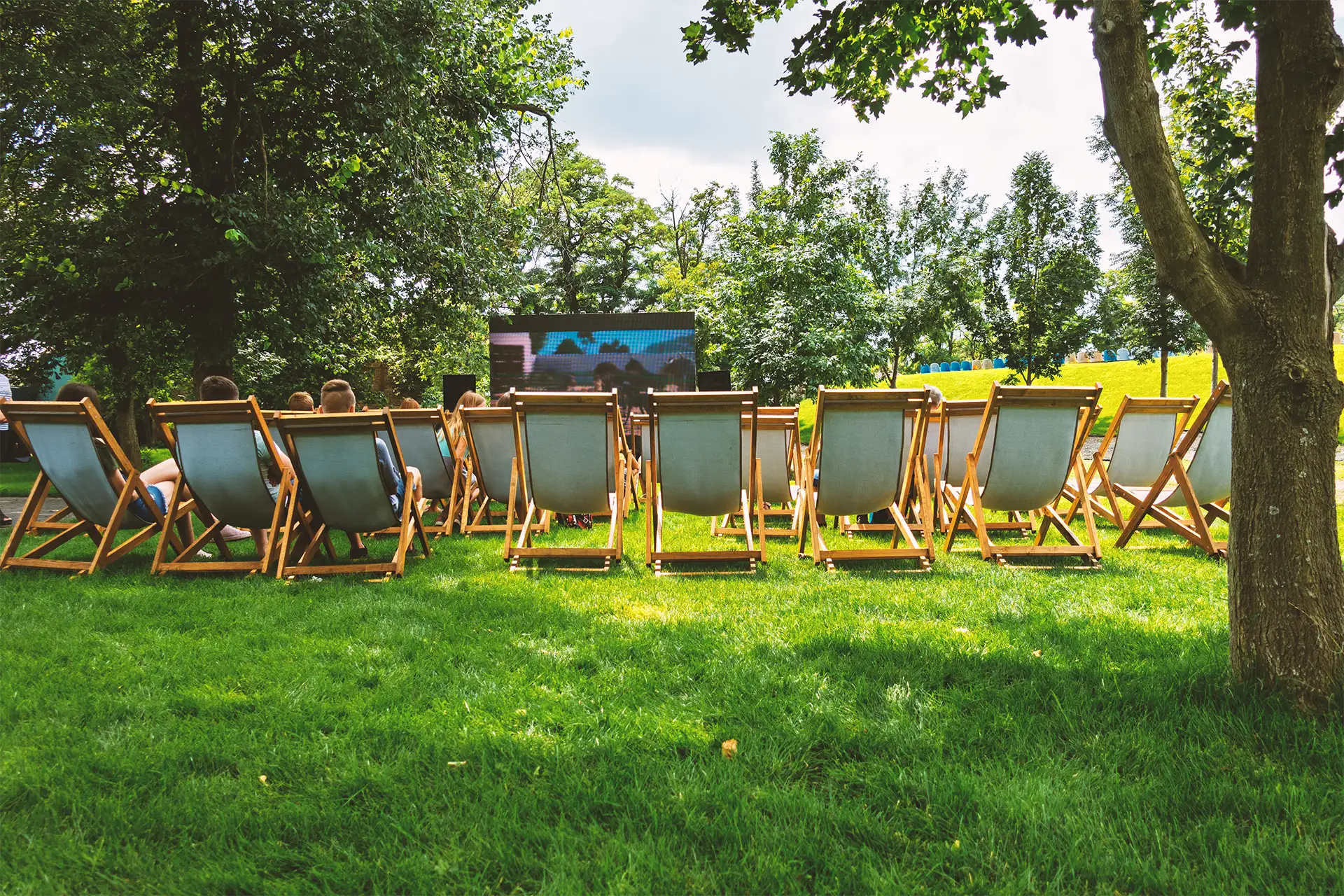 A backyard projector screen setup during the day with rows of lawn chairs set up for viewing