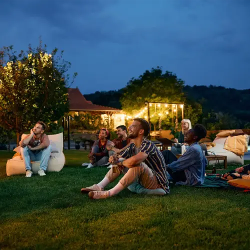 A group of friends watching football on a projector screen in a backyard at night
