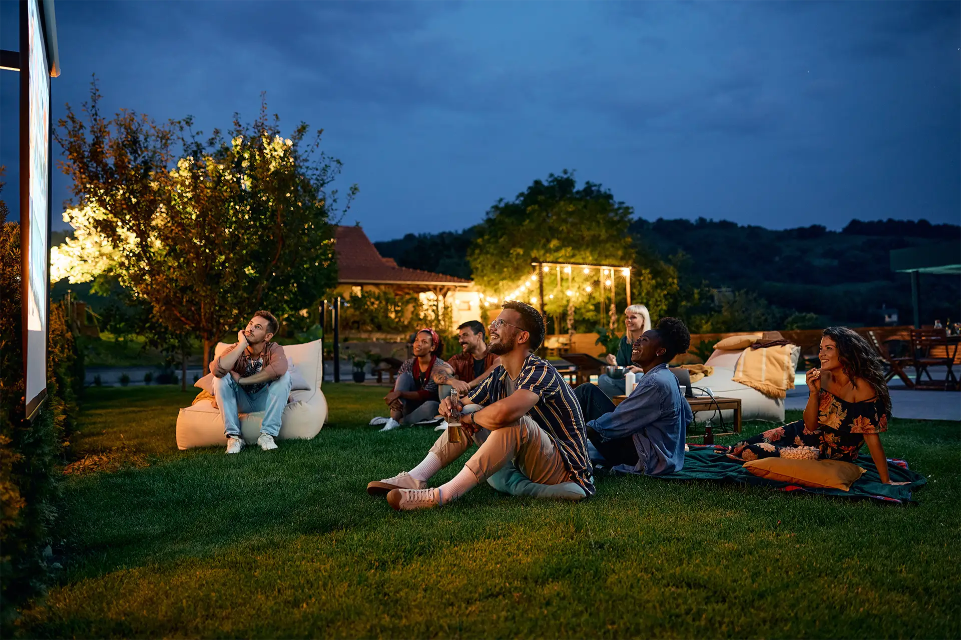A group of friends watching football on a projector screen in a backyard at night
