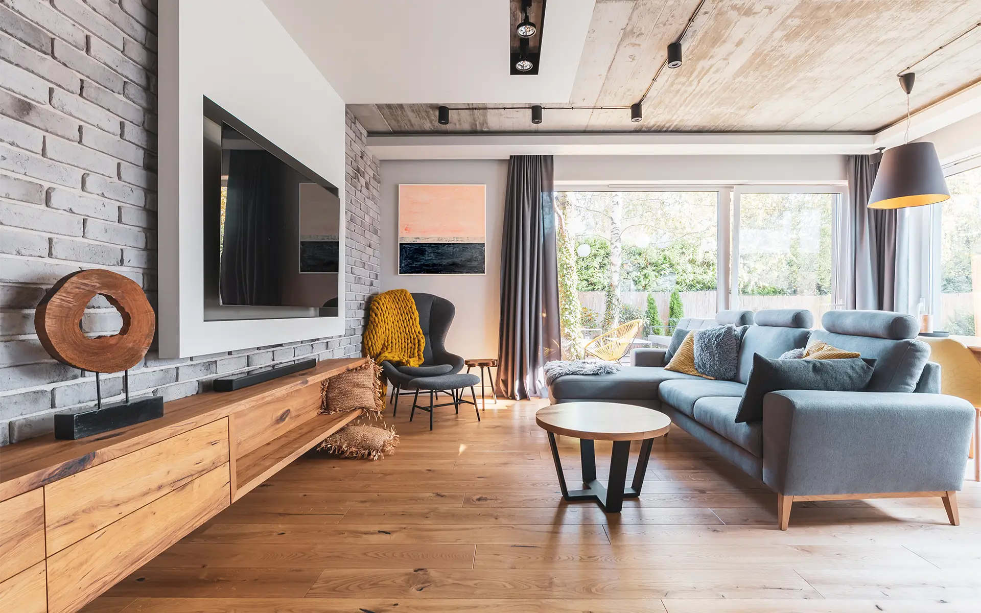 Elegant living room with a light wooden floor, a modern grey sectional, and a feature wall with a TV cleanly embedded within
