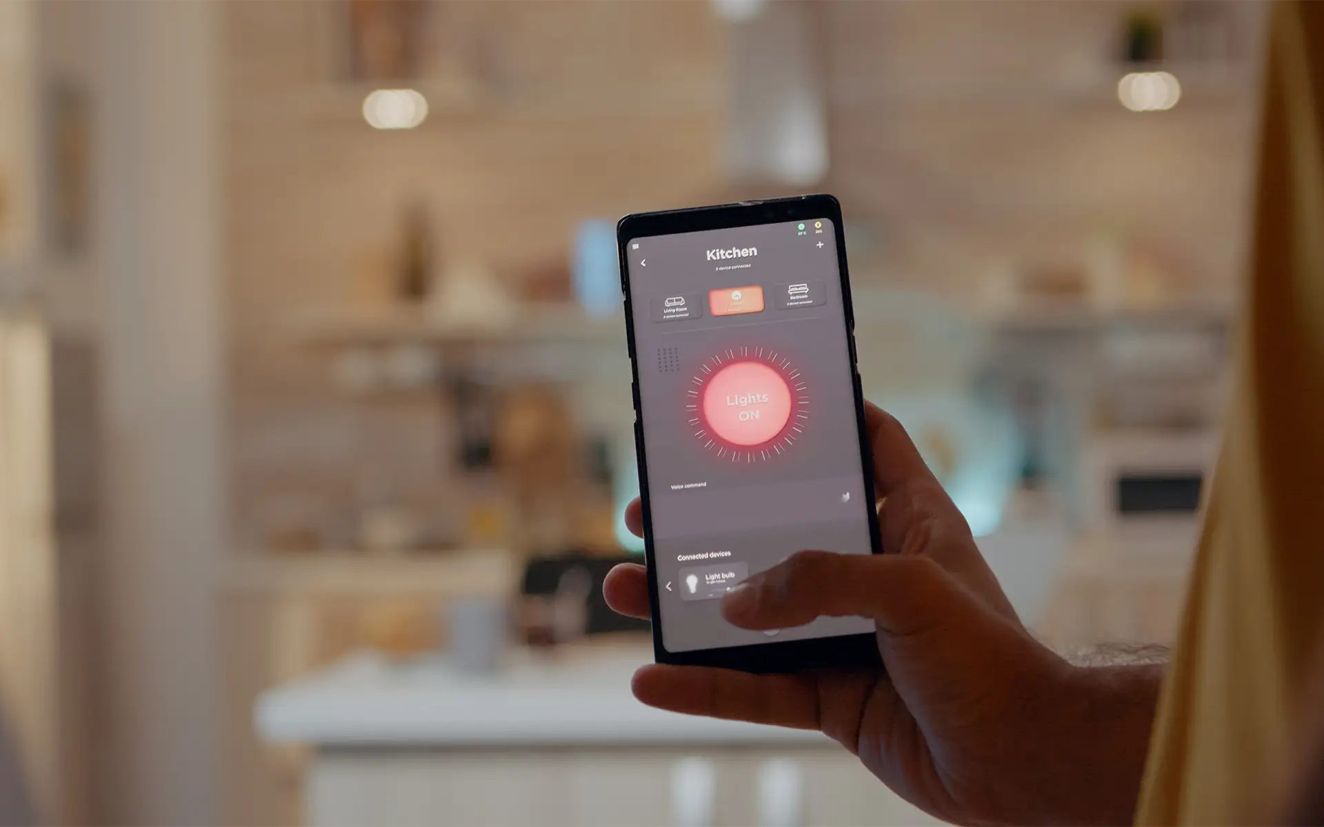 A man stands in his kitchen while using his smart home control app on his phone to adjust the lights