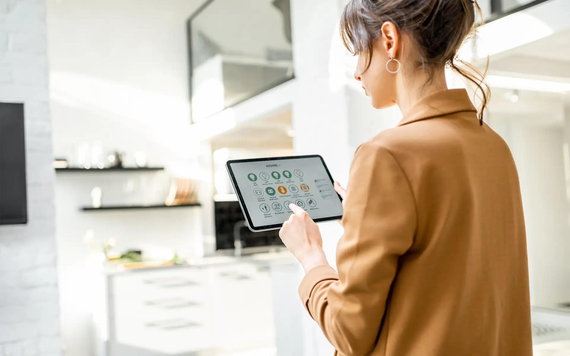 A woman stands in her sunny, white living room, using a tablet to control her smart home automation with the control system app